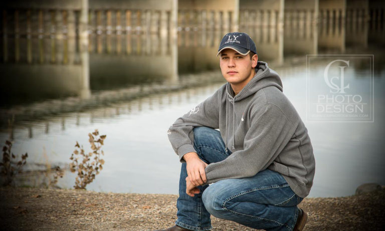 Senior boy in a blue hat and grey hoodie in front of a river
