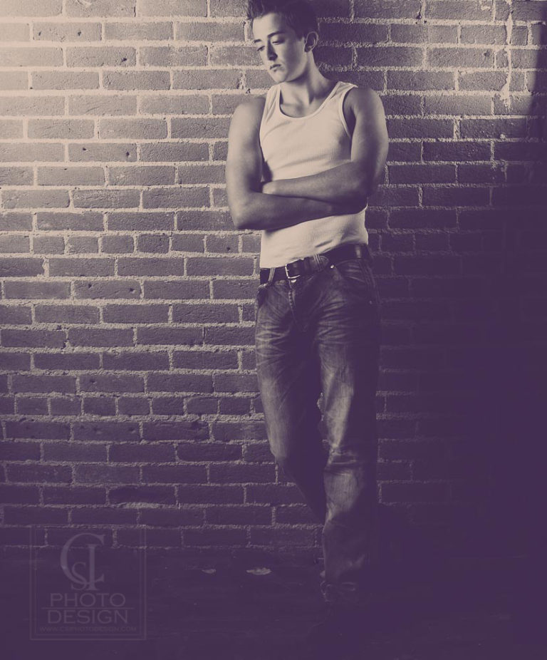 Senior boy in white tank top jean in front of a brick wall