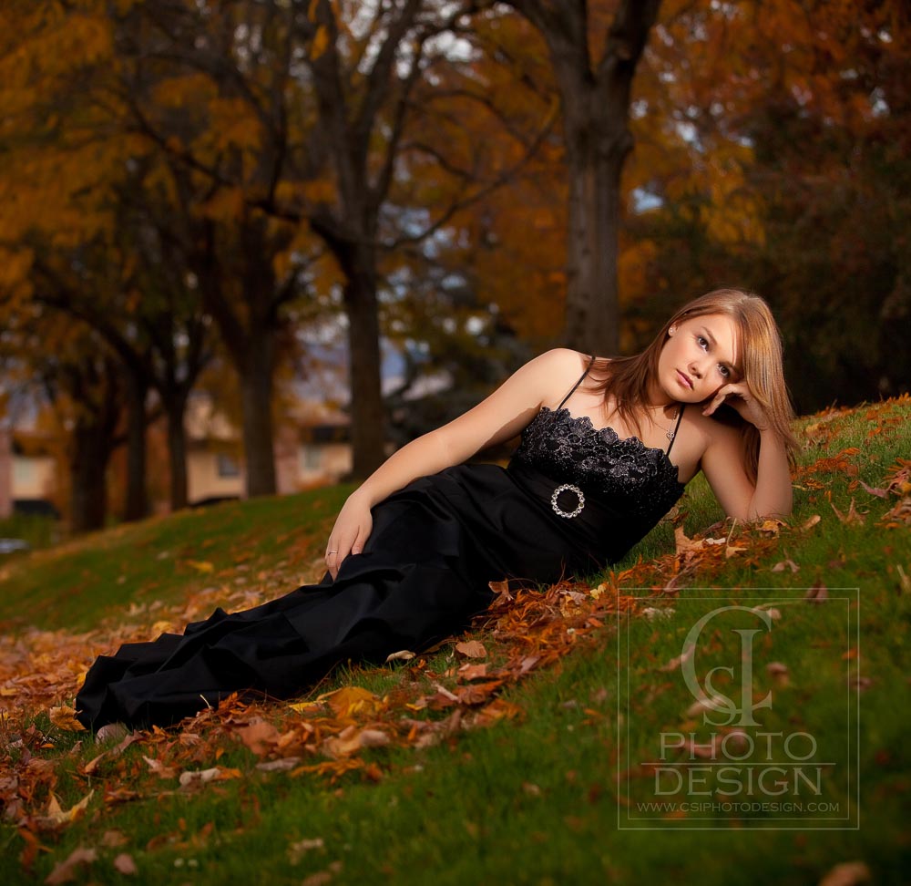 Senior girl in black prom dress lying in fall leaves