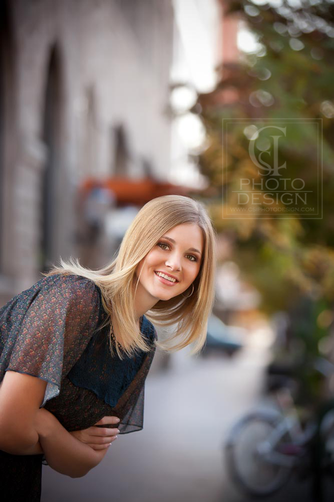 Senior girl leaning into the frame with sidewalk background