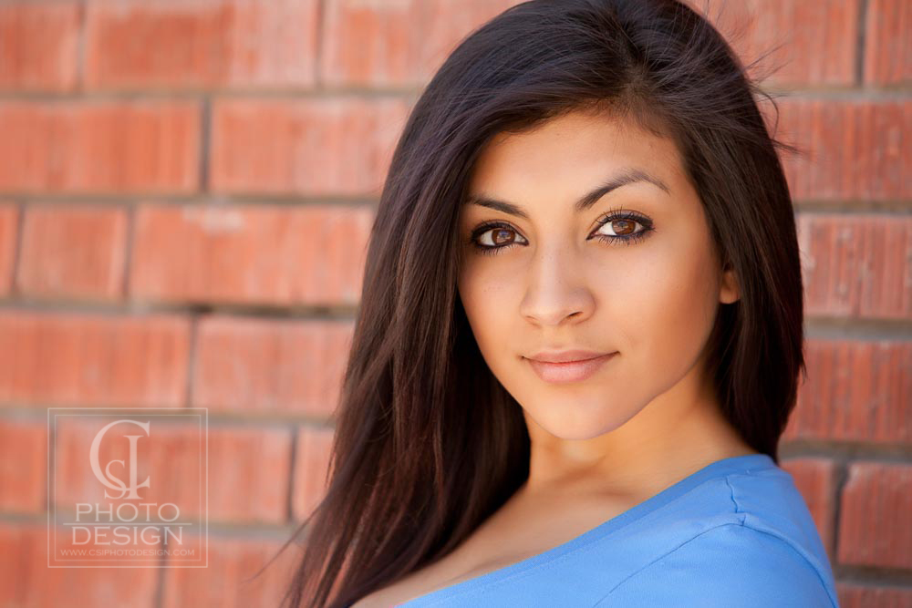 Senior girl in a blue top against a red brick background